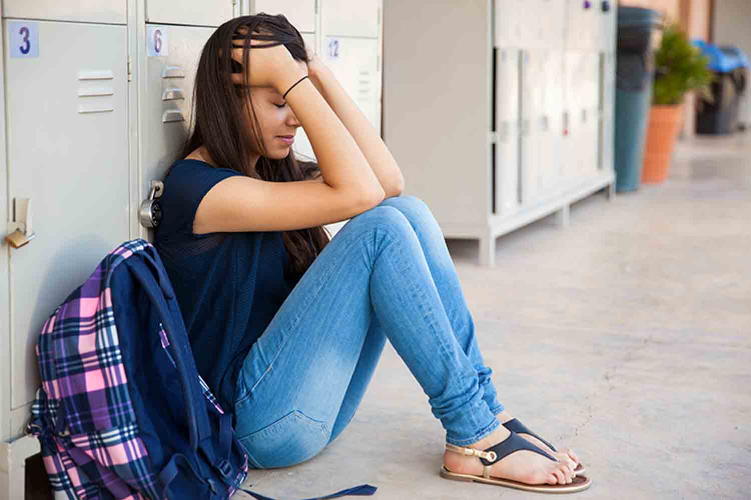 Une adolescente est assise par terre en se tenant les mains. Elles souffre de décrochage scolaire